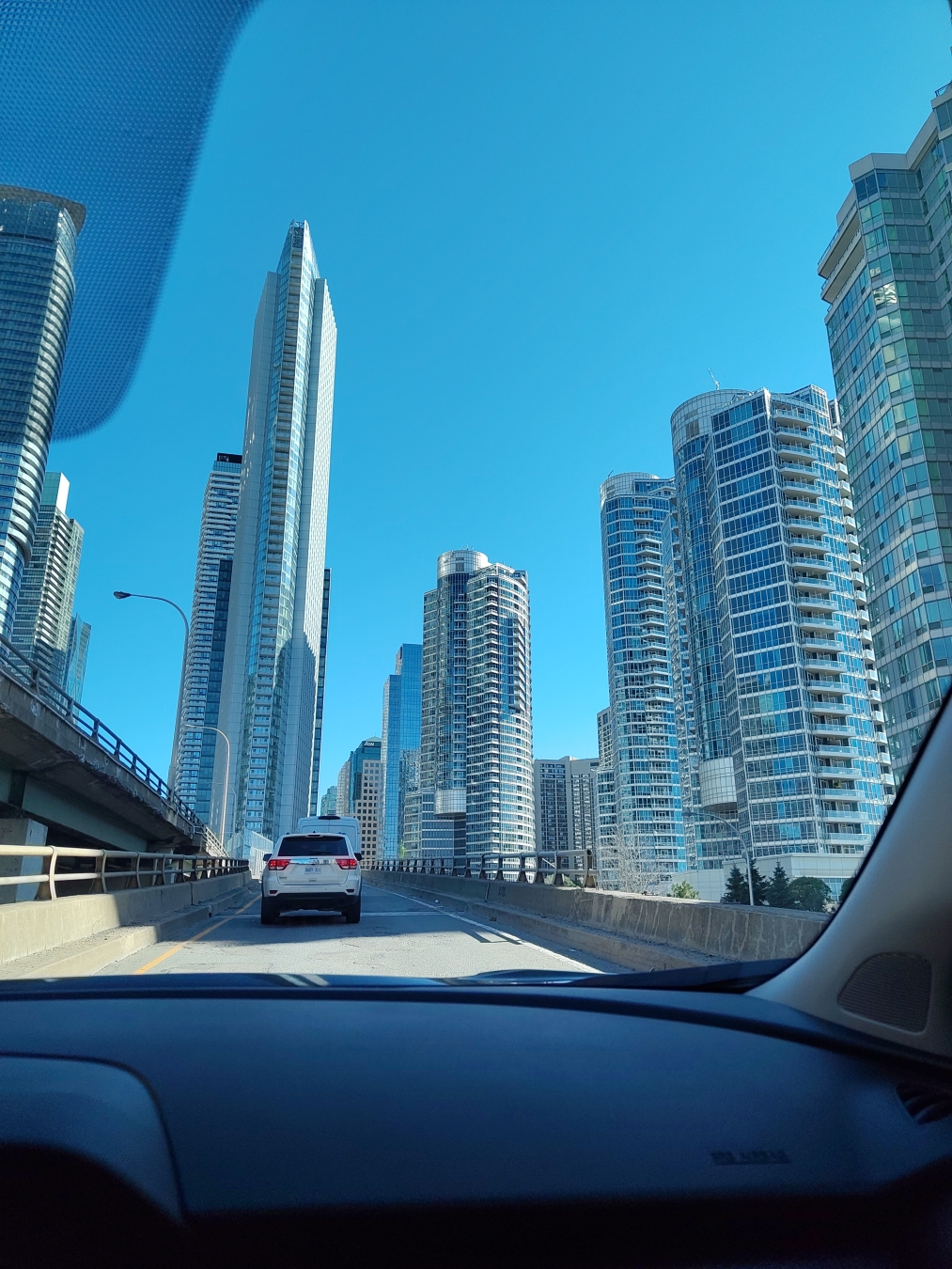 Photo prise depuis le siege passager d'une voiture roulant sur route entourée de grattes-ciel de plusieurs dizaines d'étage chacun.