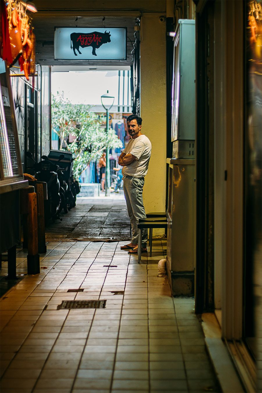 an hallway in the central market of Athens. We see a man arms crossed looking at the camera. Above him a sign with a cow.