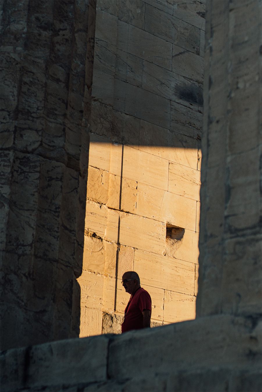 Between two collums of a temple a silhouette of a man, a ray of light is lightning the wall of the temple behind him .