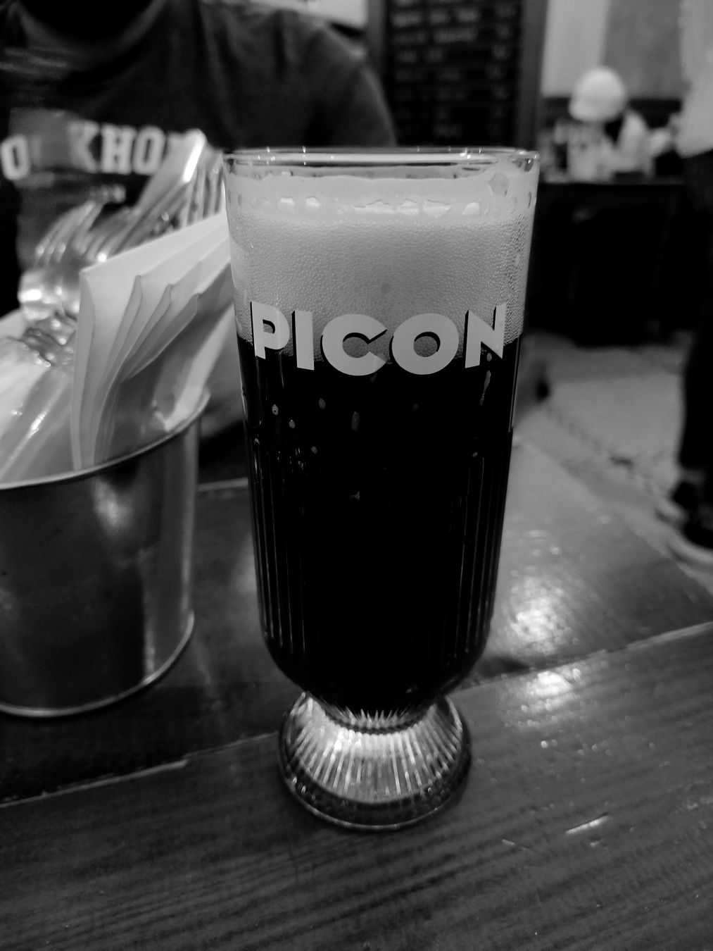 pose sur une table, un verre empli de picon bière a côté un ramequin avec serviettes et couvert