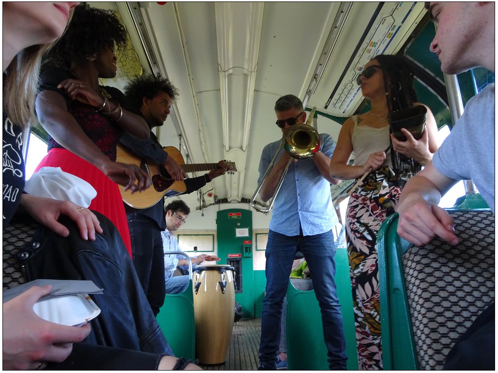 Un groupe de musique joue dans un wagon. Une chanteuse, un guitarisete, un tromboniste et  deux percussionistes (un congas et une cloche) sont pris sur le vif.